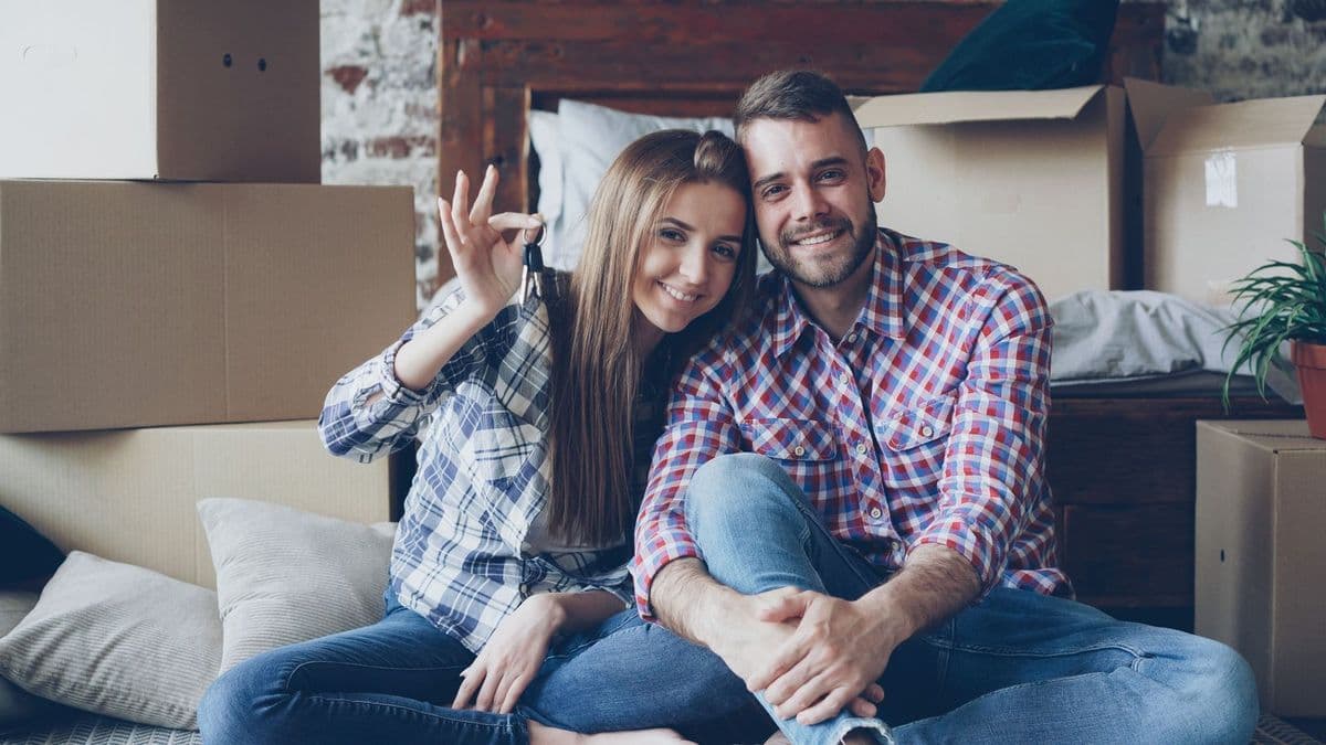 A happy young couple holding the keys to their first home, surrounded by moving boxes.