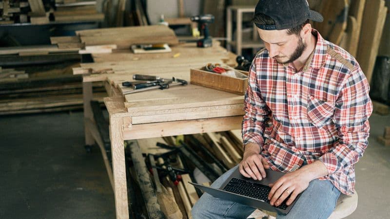 A self-employed tradesperson using a laptop in their workshop
